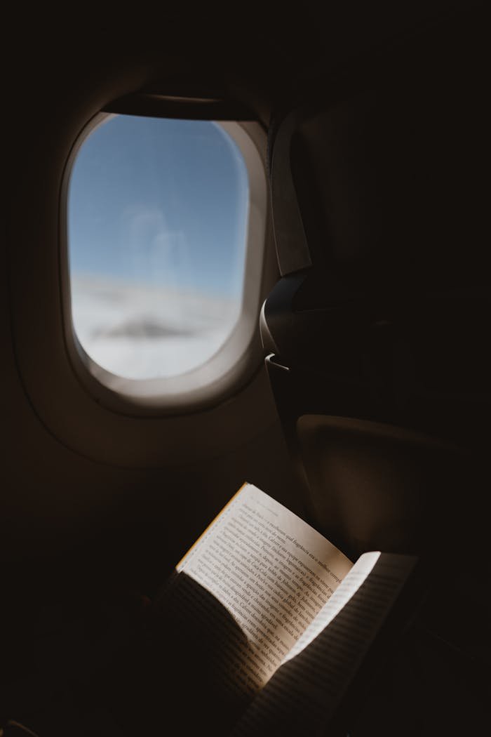 A peaceful moment reading by an airplane window with a view of the sky, capturing the essence of travel.