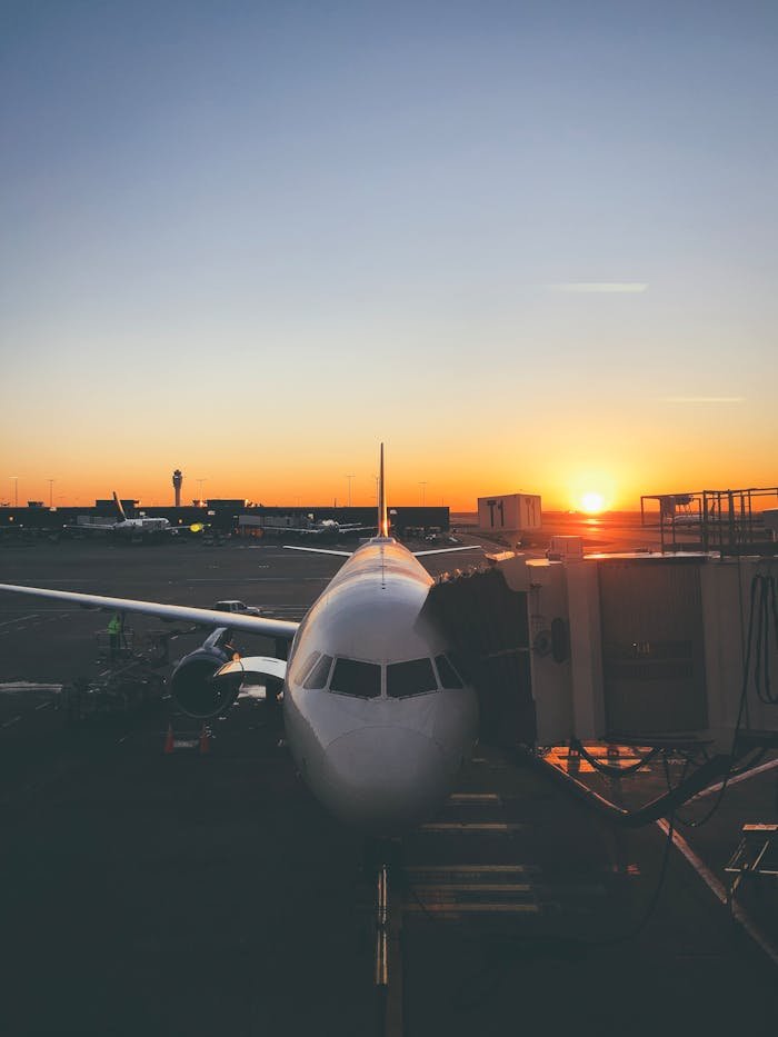 A commercial airplane docked at an airport gate as the sun rises, casting a golden glow.