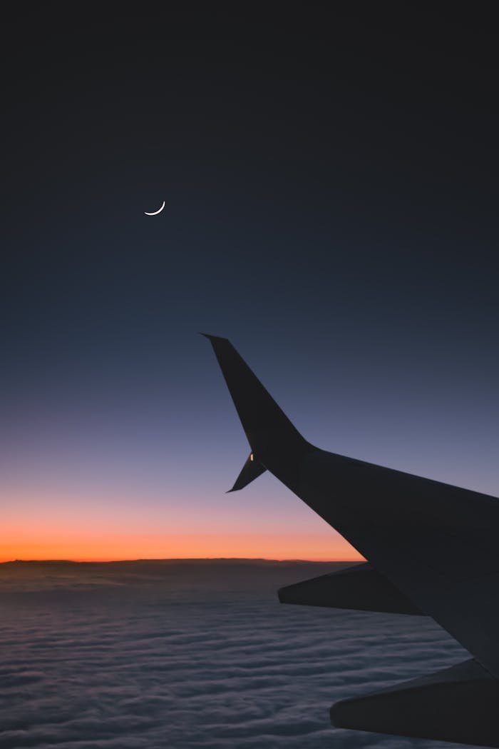 A stunning view of an airplane wing silhouetted against a twilight sky featuring a crescent moon.
