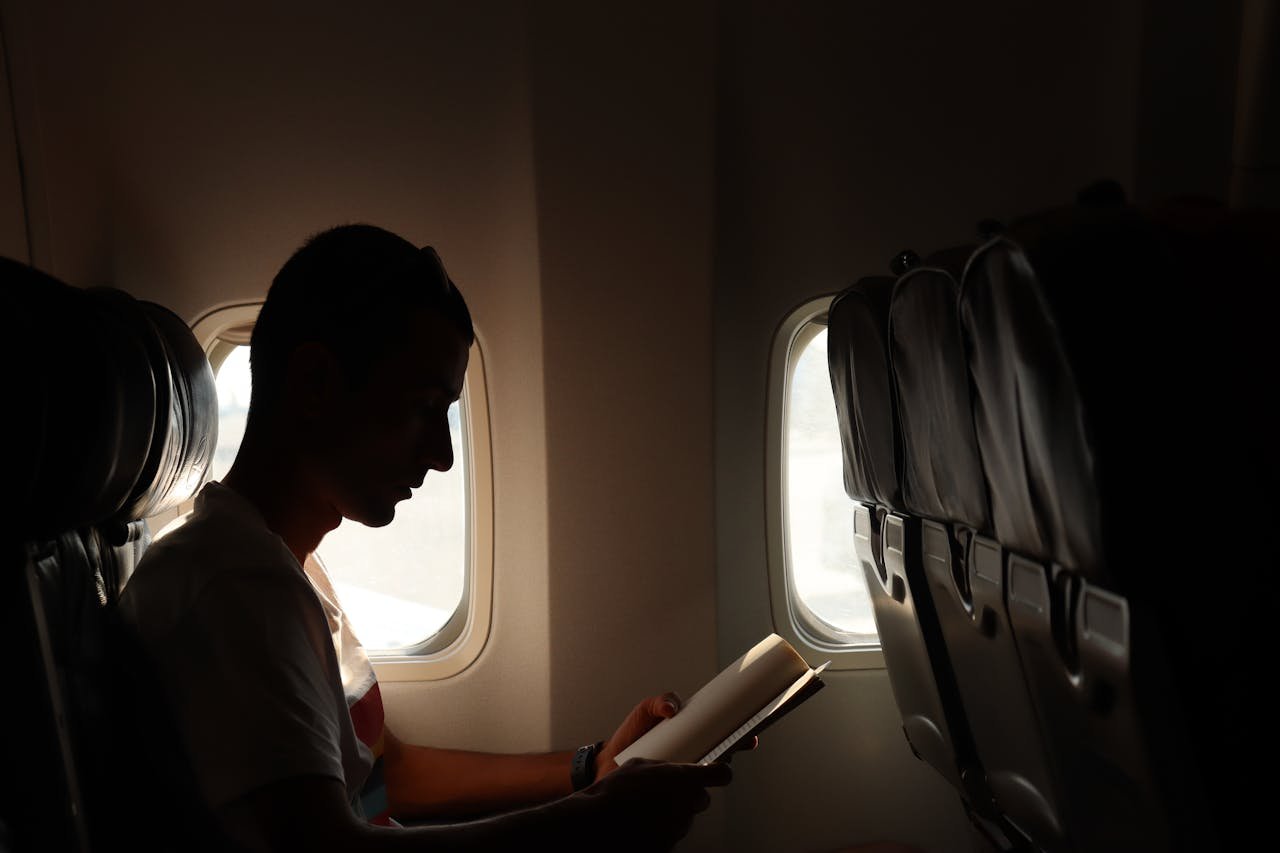 A man reading a book by the window, captured in a silhouette during flight.